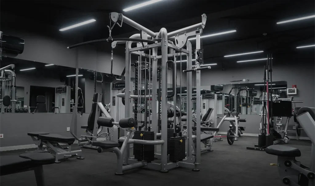 Open gym floor with plate-loaded machines, benches and a cable station