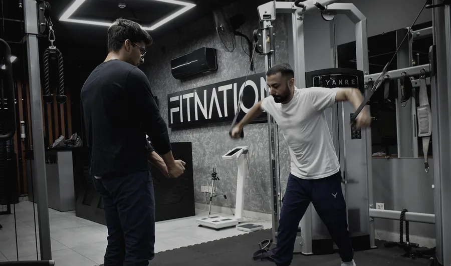 Coach watching a member work on the cable machine beside the Fitnation sign